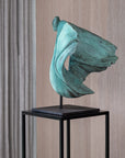 Teal abstract sculpture on a black stand against a wooden paneled wall.