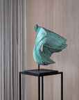 Teal abstract sculpture on a black stand against a wooden paneled wall.