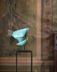 Decorative wall with classical painting and a teal flower on a stand.