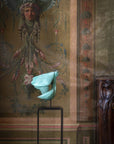 Decorative wall with classical painting and a teal flower on a stand.