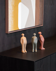 Three ceramic figures on a dark surface with a abstract painting in the background