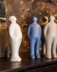 Four Gardeco Ceramic Sculpture Visitor Small Sand Cor02, selected by Guido Deleu, are delicately arranged on a shelf, adding a warm presence and enhancing the decor alongside a captivating painting.