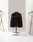 Black jacket on a coat stand with gold and silver hangers against a neutral background