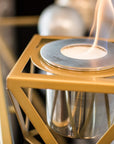Gold hexagonal bioethanol fireplace with a small flame inside, blurred background
