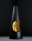 A modern black cone-shaped fireplace with a curved gold-toned glass front and a visible flame, set against a dark studio background.