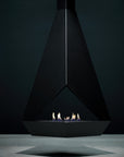A modern black triangular indoor bioethanol fireplace with a glass wind guard and small flames burning inside, set against a dark charcoal background.