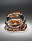 A amber and clear finish glass sculpture from Glasremis on a grey background available at Spacio retail store in Mumbai