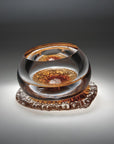 A amber and clear finish glass sculpture from Glasremis on a grey background available at Spacio retail store in Mumbai