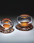 Two glass sculptures from Glasremis of Lithuania with amber-colored interior on a gradient background available at Spacio retail store in Mumbai.