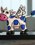 Colorful cow figurine with blue and black patterns on a wooden surface