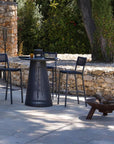Outdoor patio setting with black chairs, table, and fire pit against a stone wall.