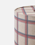 Close-up of a cylindrical lampshade or fabric-covered cylindrical object with a plaid pattern in beige, red, and blue on a white background.
