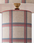 Close-up of a table lamp shade and upper lamp base featuring a beige linen-like fabric with a red and blue plaid pattern, plus a brass-toned finial.