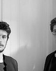 A black and white photo of two men standing next to each other, with an Italamp Dali Chandelier hanging in the background.