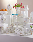 Jonathan Adler Gilded Muse Eve Fruit Bowl on a white pedestal with Muse collection vases and mugs – porcelain artistry available at Spacio India.