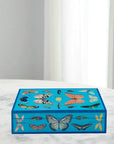 Jonathan Adler Large Lacquer Botanist Box placed on marble surface with colourful butterfly artwork – stylish storage from Spacio India.