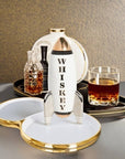 Jonathan Adler Rocket Whiskey Mid-Century Decanter displayed in a stylish bar setting with a glass of whiskey, available at Spacio India retail stores and online. A high-fired white porcelain decanter with gold and silver detailing.