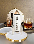 Jonathan Adler Rocket Whiskey Mid-Century Decanter displayed in a stylish bar setting with a glass of whiskey, available at Spacio India retail stores and online. A high-fired white porcelain decanter with gold and silver detailing.