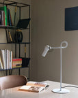 Modern desk lamp on a table with a bookshelf and wall in the background