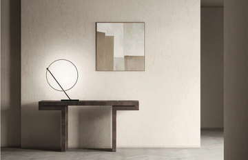 A KDLN Poise Table Lamp emits a circle of light, illuminating a painting on the wall.