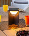 Table setting with a modern solar table lamp, colorful glasses, and fruit on a wooden table.