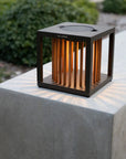 Modern outdoor solar lantern on a concrete surface with greenery in the background