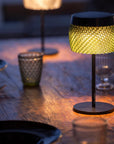 Small table lamp with woven design on a wooden surface with glasses and plates.
