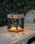 Wooden solar table lamp with a glowing interior on a rustic wooden surface by Les Jardins available at Spacio retail stores in Mumbai & Kolkata.
