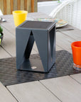 Modern grey outdoor solar lantern on a wooden table with colourful glasses and fruit.