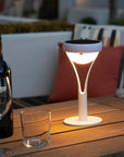 Solar-powered outdoor lamp on a wooden table with a bottle and glass, set against a blurred outdoor background.