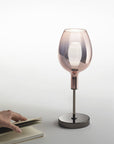 Goblet-shaped table lamp on a white surface with a hand holding a book.