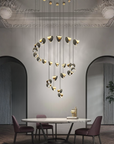 A modern multi-light pendant chandelier with gold and black sculptural leaf-like shades hangs over a dining table in a stylishly decorated dining room with arched doorways and a potted plant.