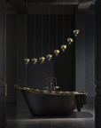 A luxury freestanding bathtub in matte black with polished gold trim and fixtures, set in a dark, elegant bathroom with patterned wallpaper and hanging pendant lights.