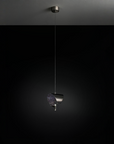 A modern pendant light fixture with a dark metallic cylindrical shade and a textured, glittery purple glass shade, suspended by a thin cord from a matching ceiling canopy against a dark background.