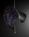 A modern sculptural pendant light with a glossy black metal frame and a dark starry galaxy-patterned interior, shown against a dark gradient background.