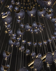 A luxury multi-light chandelier featuring numerous teardrop-shaped pendant lights with textured navy blue and gold speckled glass, suspended from a dark ceiling by thin cables.