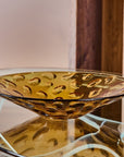 Amber crystal bowl on a reflective surface with a blurred background