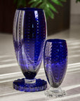 Two blue crystal vases on a reflective surface with a blurred background