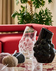 Decorative crystal vases and yarn balls on a table with a red sofa and plant in the background