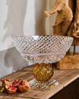 Decorative crystal bowl on a wooden surface with pomegranates and a piece of driftwood.