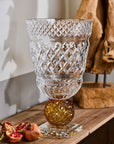 Decorative crystal vase on a wooden surface with pomegranates and a textured wall in the background