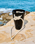Black crystal cup tied with rope on a rock with ocean in the background