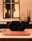 Black decorative crystal vase on a wooden table with framed art in the background