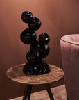 Black abstract crystal sculpture on a marble table against a brown wall with a pink chair.