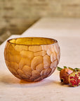 Decorative crystal bowl with textured surface on a wooden table with pomegranate and leaves.
