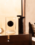 Mario Cioni A.Y.L.I. Cilindric Black Crystal Vase by Tondo Doni on a side table with a vase & table clock in bedroom interior available at spacio india for luxury home decor collection of decorative vases.
