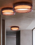 Three modern flush-mount ceiling lights with textured bronze metal rims and warm glowing white interiors, installed on a curved plaster ceiling in a minimalist interior setting.