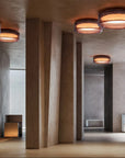 Modern minimalist interior space with textured concrete walls and ceiling, featuring multiple round flush-mount ceiling lights with dark metallic rims and warm glowing light diffusers.