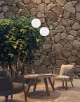 Outdoor seating area with round pendant lights from Masiero, wicker chairs and a wooden table against a stone wall.