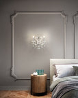 Aqaba crystal chandelier by Masiero from Spacio on a wall behind a neatly made bed with a wooden side table